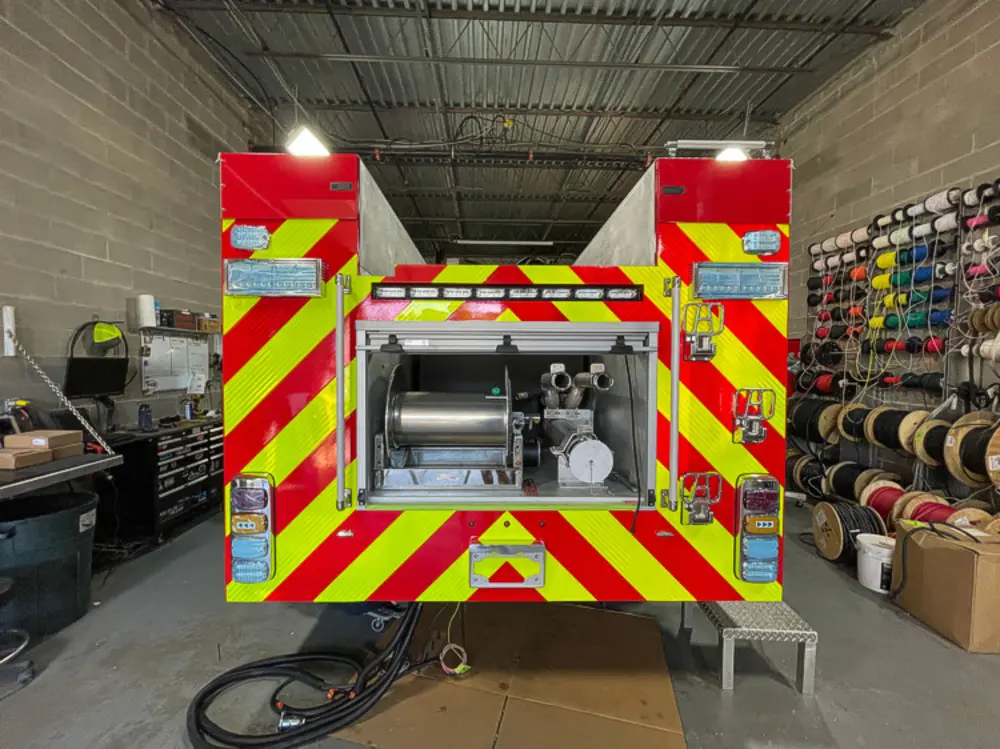 Exterior view of small fire truck showing cab, body compartments, and wheel/tire area.